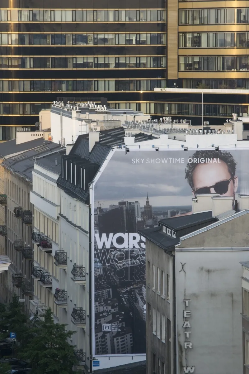 Tall WARS billboard rising between historic rooftops and modern towers